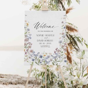 May include: A white wedding welcome sign with a floral border. The sign reads "Welcome to the wedding of Sophie Hooper and David Robert 08/10 20XX 123 Anywhere St. Any City, ST 12345".