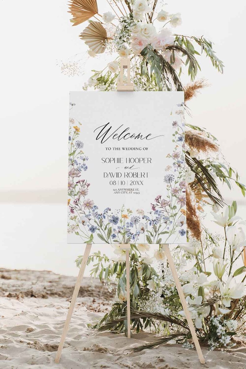 May include: A white wedding welcome sign with a floral border. The sign reads "Welcome to the wedding of Sophie Hooper and David Robert 08/10 20XX 123 Anywhere St. Any City, ST 12345".