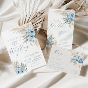 May include: A set of three wedding invitation cards with a blue and white floral design. The cards include the wedding invitation, a details card, and a RSVP card. The cards feature a watercolor floral design with blue flowers and white pampas grass.