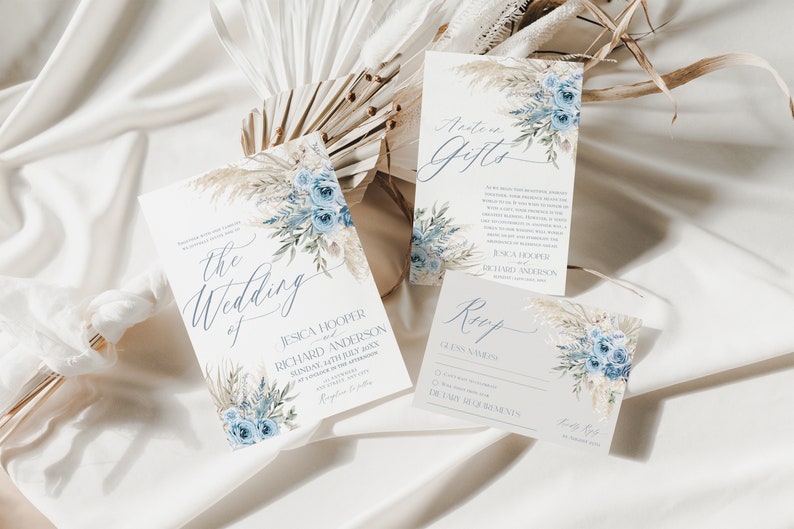 May include: A set of three wedding invitation cards with a blue and white floral design. The cards include the wedding invitation, a details card, and a RSVP card. The cards feature a watercolor floral design with blue flowers and white pampas grass.