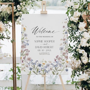May include: A white wedding welcome sign with a floral design featuring blue, pink, and yellow flowers. The sign reads "Welcome to the wedding of Sophie Hooper and David Robert 08/10/20XX 123 Anywhere St, Any City, ST 12345".