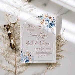 May include: A rectangular wedding invitation card featuring a floral arch design with blue and beige flowers, pampas grass, and the text Jessica Hopper & Richard Anderson. A gold wax seal stamp is positioned to the left of the invitation.