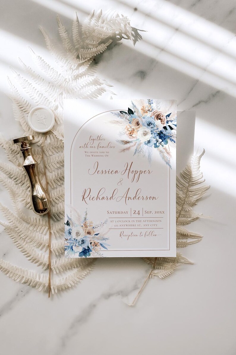 May include: A rectangular wedding invitation card featuring a floral arch design with blue and beige flowers, pampas grass, and the text Jessica Hopper & Richard Anderson. A gold wax seal stamp is positioned to the left of the invitation.