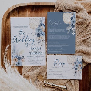 May include: A wedding invitation suite with a blue and beige color scheme. The invitation features a floral design with pampas grass and the text "The Wedding of Sarah and Thomas". The details card includes information about the wedding reception and directions. The RSVP card has a place for guests to indicate their attendance.