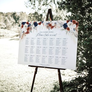 May include: A white wedding seating chart with a floral design in shades of red, blue, and white. The chart lists tables 1 through 21 and includes the text "Our Favorite People Please Take a Seat".