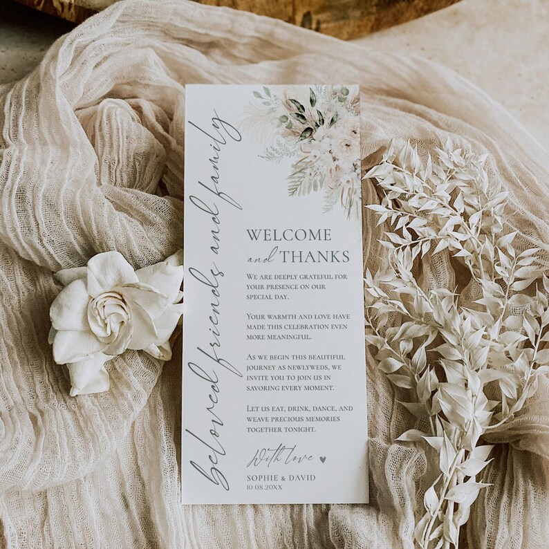 May include: A vertical white wedding programme card featuring a floral illustration at the top and the text: Beloved friends and family, Welcome and Thanks, We are deeply grateful for your presence on our special day, Sophie & David 10.08.20XX.