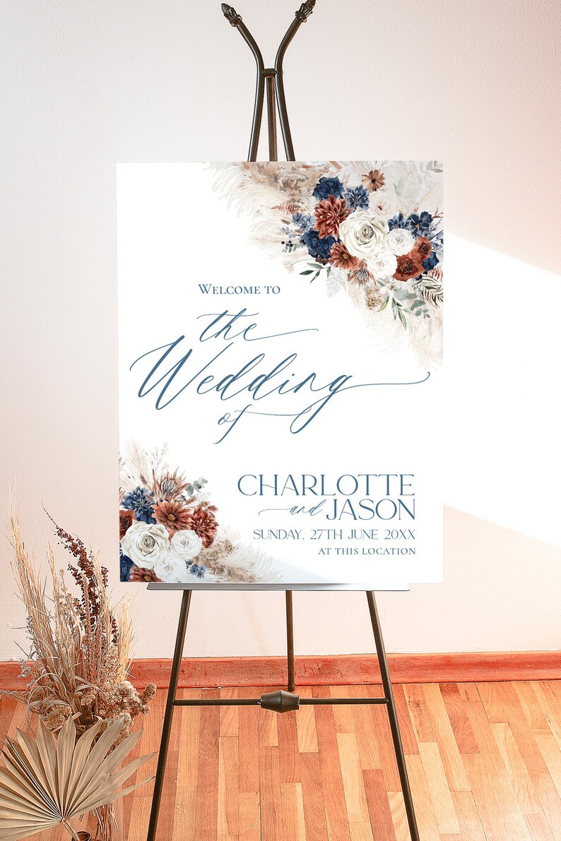 May include: Welcome to the wedding of Charlotte and Jason, a wedding sign with a floral design in shades of blue, white, and rust. The sign is on a wooden easel and the text is in a blue font.