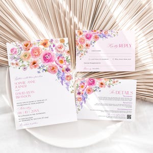 May include: A wedding invitation suite featuring a main invitation, a response card, and a details card. Each white card is decorated with watercolor floral illustrations in shades of pink, orange, and purple, with printed text in pink and black ink.