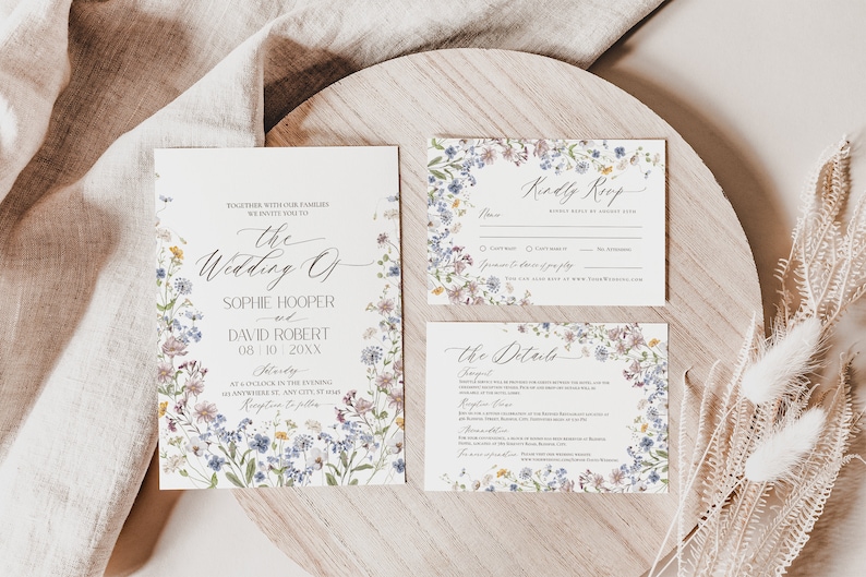 May include: Wedding invitation suite with a floral design. The invitation features a wreath of wildflowers in shades of blue, purple, and pink. The text reads "The Wedding of Sophie Hooper and David Robert 08/10 20XX". The RSVP card features a similar floral design and the text "Kindly RSVP". The details card features the same floral design and the text "The Details".