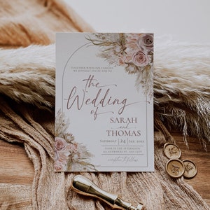 May include: A rectangular wedding invitation card featuring a floral arch design with muted pink roses and dried grasses. The text reads: The Wedding of Sarah and Thomas, Saturday 24 Sep, 20xx, Four in the afternoon, 123 Anywhere St., Any City, reception to follow.