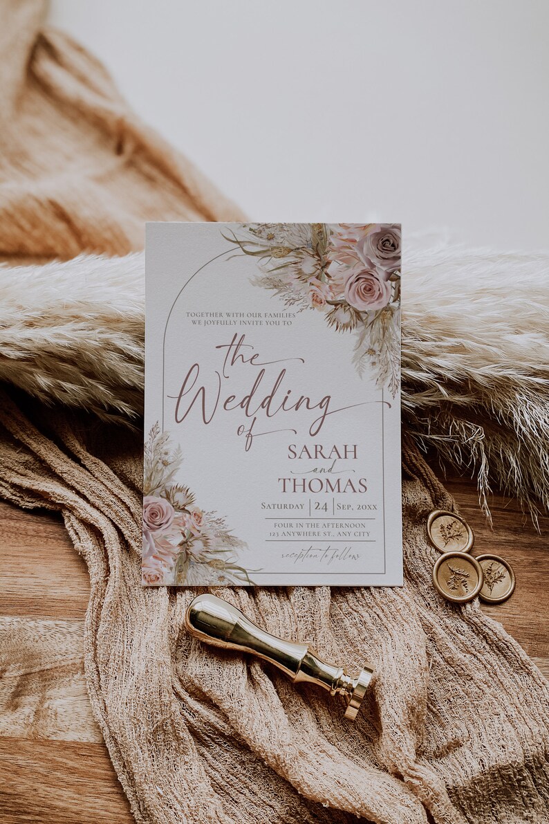 May include: A rectangular wedding invitation card featuring a floral arch design with muted pink roses and dried grasses. The text reads: The Wedding of Sarah and Thomas, Saturday 24 Sep, 20xx, Four in the afternoon, 123 Anywhere St., Any City, reception to follow.
