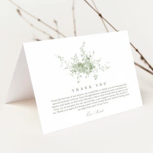 May include: White folded thank you card with a floral design in shades of green. The card features the words "THANK YOU" at the top, with a message below. The card is blank inside.
