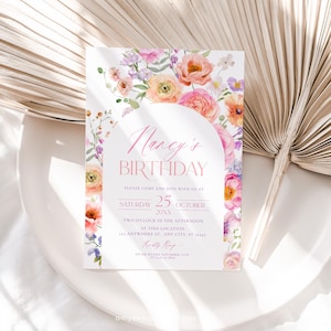 May include: A floral birthday invitation with a pink and white color scheme. The invitation features a watercolor floral arch with pink, orange, and purple flowers. The text on the invitation reads "Nancy's Birthday" and includes the date, time, and location of the event.