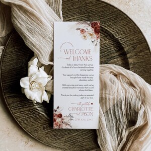 Puede incluir: Una tarjeta de bienvenida rectangular blanca para bodas con ilustraciones florales en tonos burdeos y crema. El texto dice: Welcome and Thanks, Today is about more than just us, Charlotte and Jason, 27th June 20XX, with gratitude.