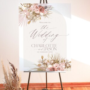 May include: Welcome to the wedding of Charlotte and Jason, a wedding sign with a floral design featuring dried pampas grass, blush pink roses, and gold accents.