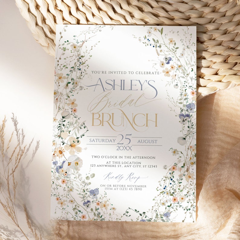 May include: A floral-themed bridal brunch invitation with a wreath of watercolor flowers in shades of blue, white, and pink. The text reads "You're invited to celebrate Ashley's Bridal Brunch, Saturday 25 August 20XX, Two o'clock in the afternoon at this location 123 Anywhere St., Any City, ST 12345, Kindly RSVP on or before November 15th at (123) 45 7890."