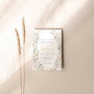 May include: A floral-themed bridal brunch invitation with a white background and a wreath of watercolor flowers. The text reads "You're invited to celebrate Ashley's Bridal Brunch, Saturday 25 August 20XX, Two o'clock in the afternoon at this location, 123 Anywhere St, Any City, ST 12345, Katy Rep".