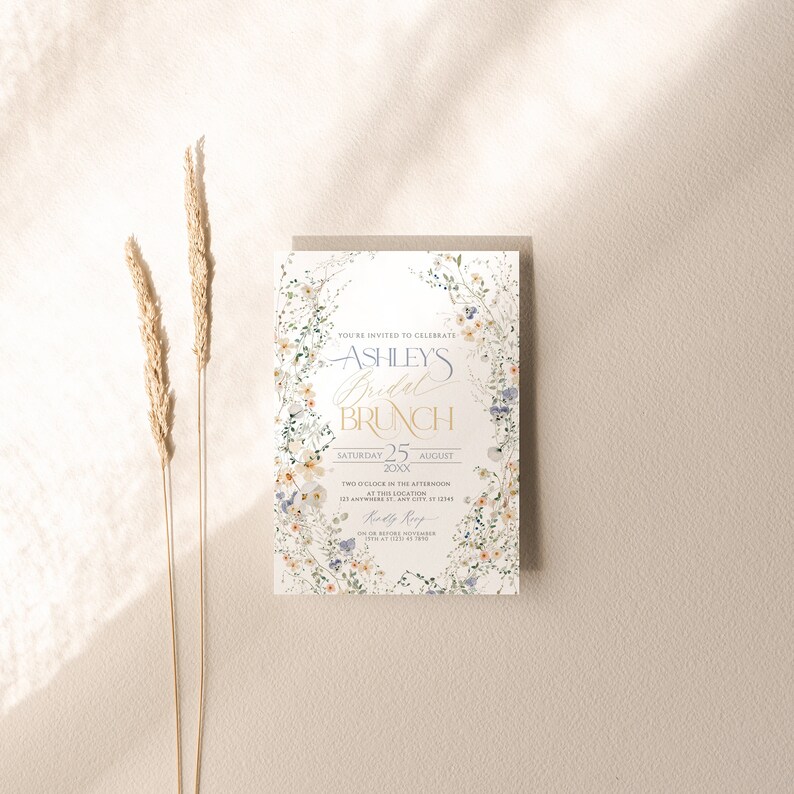 May include: A floral-themed bridal brunch invitation with a white background and a wreath of watercolor flowers. The text reads "You're invited to celebrate Ashley's Bridal Brunch, Saturday 25 August 20XX, Two o'clock in the afternoon at this location, 123 Anywhere St, Any City, ST 12345, Katy Rep".
