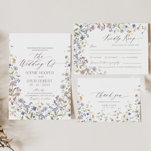 May include: A wedding invitation suite featuring a main invitation, an RSVP card, and a thank you card, all decorated with a watercolor wildflower border in shades of blue, yellow, and purple, with elegant black script and serif typography.