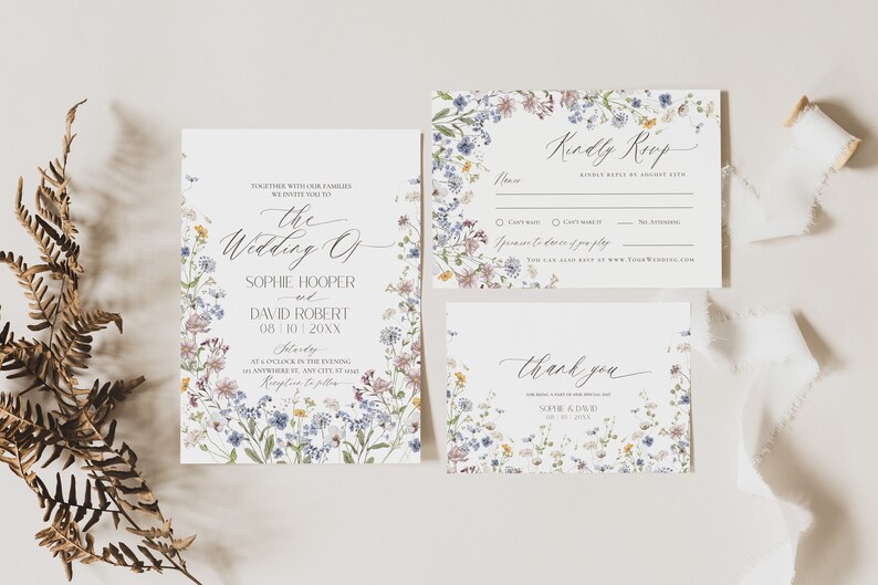 May include: A wedding invitation suite featuring a main invitation, an RSVP card, and a thank you card, all decorated with a watercolor wildflower border in shades of blue, yellow, and purple, with elegant black script and serif typography.