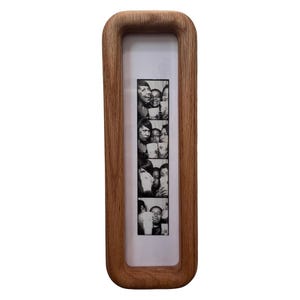 May include: A rectangular wooden photo frame with rounded edges. The frame holds a black and white photo strip featuring multiple images of people. The frame is made of light brown wood and has a white border.