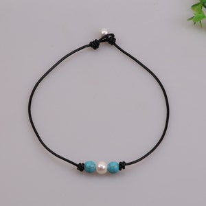 Peut inclure: Un collier ras de cou en cuir noir avec une perle blanche et deux perles turquoise.