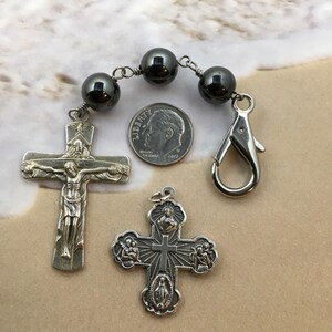 Puede incluir: Un crucifijo de plata con una figura de Jesucristo en la cruz, una cruz de plata con cinco medallones y un rosario de hematites negras con un cierre de plata. El rosario es aproximadamente del tama&ntilde;o de una moneda de diez c&eacute;ntimos de euro.