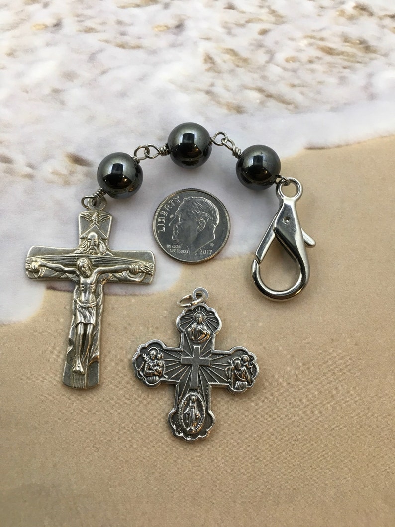Puede incluir: Un crucifijo de plata con una figura de Jesucristo en la cruz, una cruz de plata con cinco medallones y un rosario de hematites negras con un cierre de plata. El rosario es aproximadamente del tama&ntilde;o de una moneda de diez c&eacute;ntimos de euro.