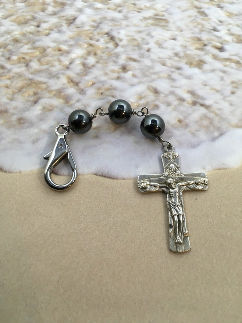 Puede incluir: Un dije de crucifijo de plata con una cadena de cuentas de hematita negra y un cierre de langosta de plata.