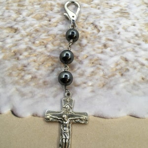Puede incluir: Una cadena de plata con un cierre de plata y cuatro cuentas negras, que termina con un crucifijo de plata con una figura de Jesucristo. El crucifijo tiene una peque&ntilde;a paloma de plata sobre la cabeza de Jes&uacute;s.