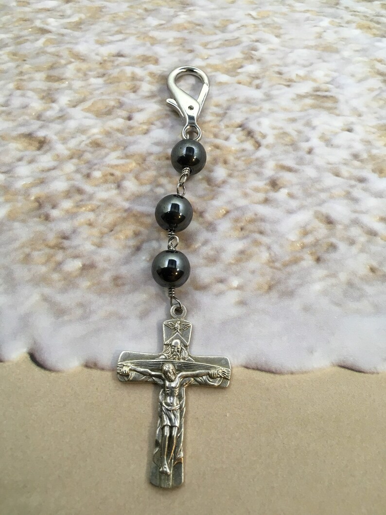 Puede incluir: Una cadena de plata con un cierre de plata y cuatro cuentas negras, que termina con un crucifijo de plata con una figura de Jesucristo. El crucifijo tiene una peque&ntilde;a paloma de plata sobre la cabeza de Jes&uacute;s.
