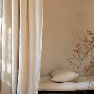 May include: A linen futon with a pillow, a beige wall, and a branch with red berries in the background.