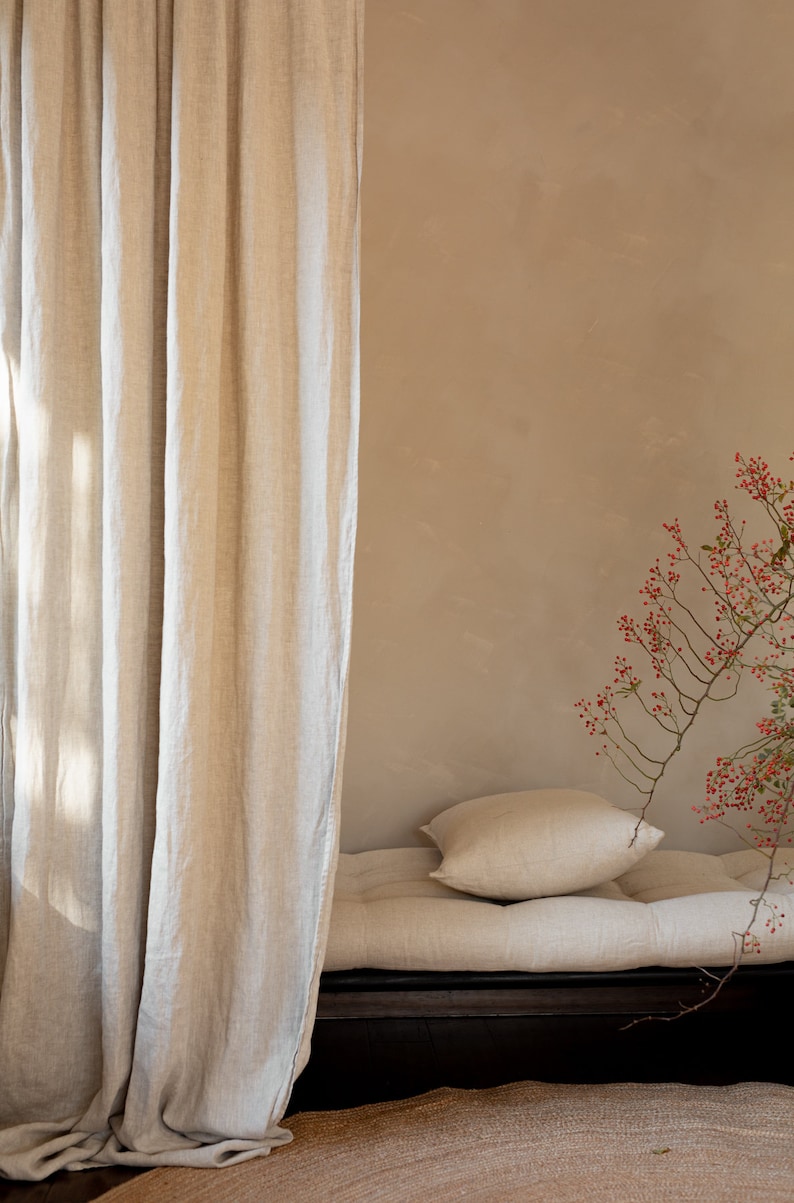 May include: A linen futon with a pillow, a beige wall, and a branch with red berries in the background.