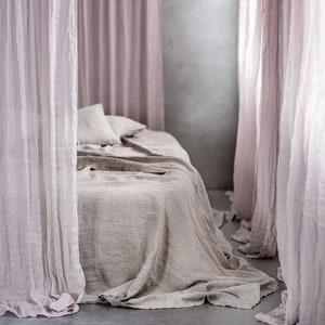 May include: A light brown linen bedspread with a light pink sheer curtain draped over the bed.