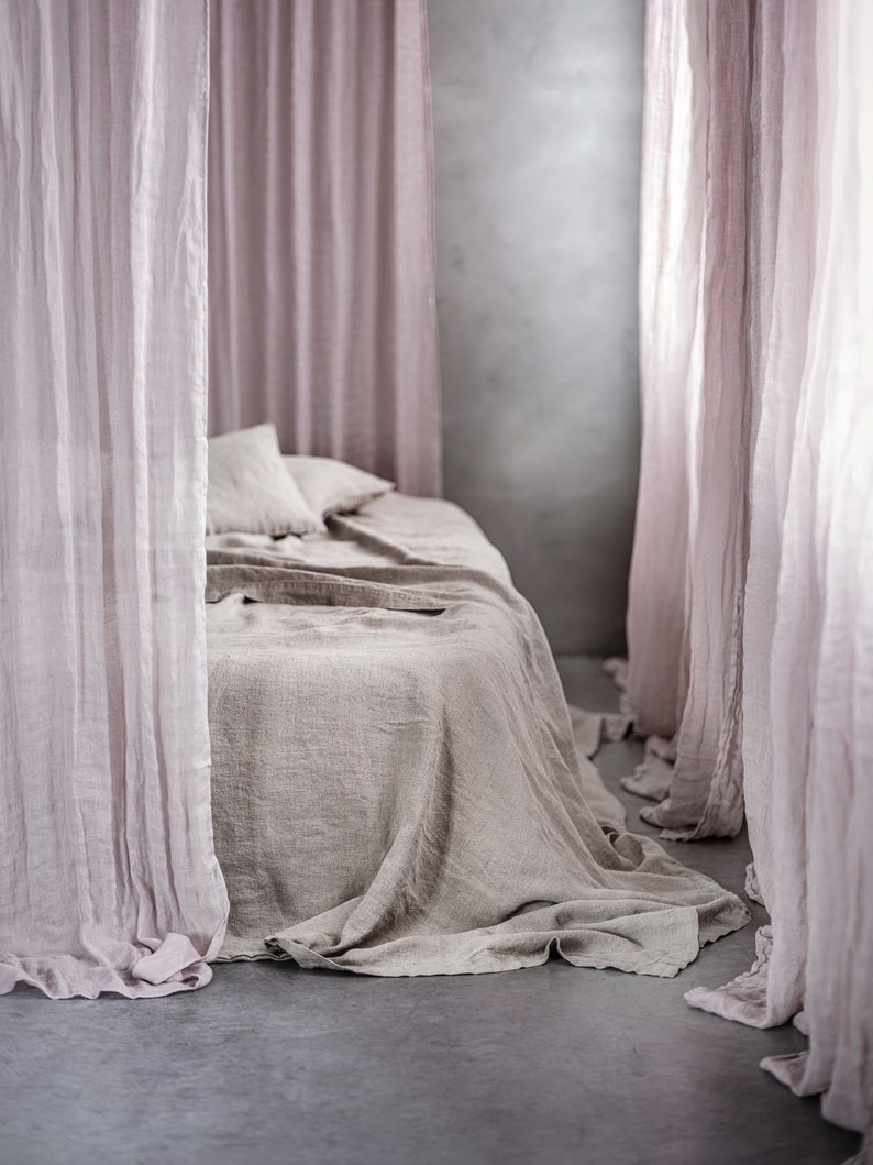 May include: A light brown linen bedspread with a light pink sheer curtain draped over the bed.