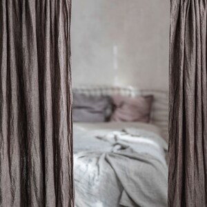 K&ouml;nnte beinhalten: Nahaufnahme eines Schlafzimmers mit einem Bett, das mit einer wei&szlig;en Bettw&auml;sche aus Leinen und Kissen bezogen ist. Das Bett ist teilweise durch zwei braune Leinenvorh&auml;nge verdeckt, die an einer schwarzen Stange h&auml;ngen.