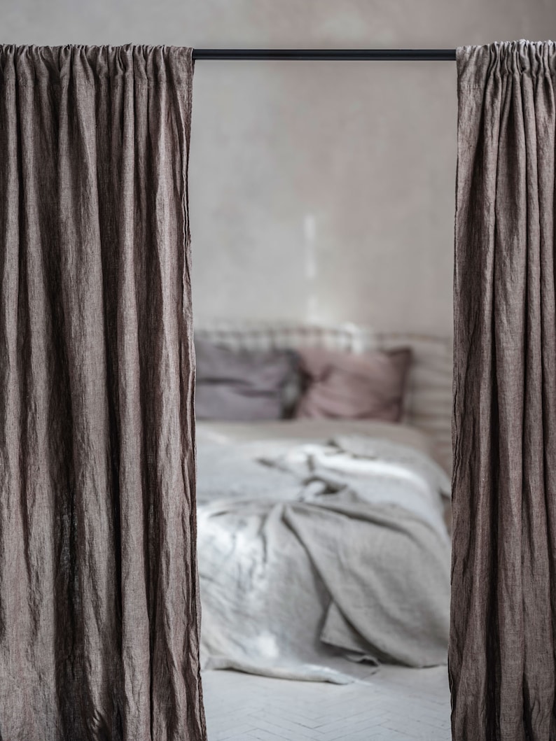 K&ouml;nnte beinhalten: Nahaufnahme eines Schlafzimmers mit einem Bett, das mit einer wei&szlig;en Bettw&auml;sche aus Leinen und Kissen bezogen ist. Das Bett ist teilweise durch zwei braune Leinenvorh&auml;nge verdeckt, die an einer schwarzen Stange h&auml;ngen.