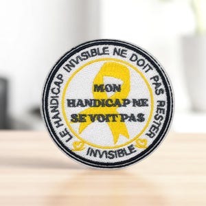 Peut inclure: Écusson brodé rond avec un ruban jaune et le texte "LE HANDICAP INVISIBLE NE DOIT PAS RESTER INVISIBLE" en noir. Le patch a un fond blanc et une bordure noire.
