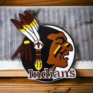 Op de afbeelding: Een geborduurde patch met een afbeelding van een Amerikaanse indiaan met een hoofdtooi, in bruin en wit. De patch heeft de tekst "Indians" in witte letters.
