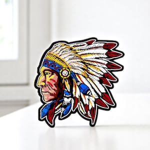 Peut inclure: Patch brodé thermocollant représentant un Amérindien de profil portant une coiffe colorée avec des plumes. Le patch est bordé de noir.
