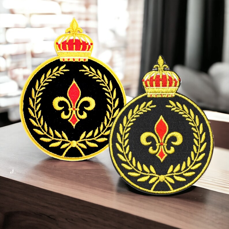 May include: Two embroidered iron-on patches with a black background, gold trim, and a red fleur-de-lis design. Each patch features a gold crown at the top.