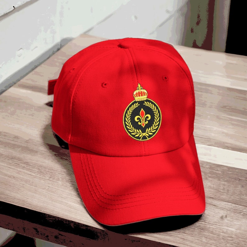 May include: Red baseball cap with a black and gold embroidered emblem featuring a crown, a fleur-de-lis, and a laurel wreath.