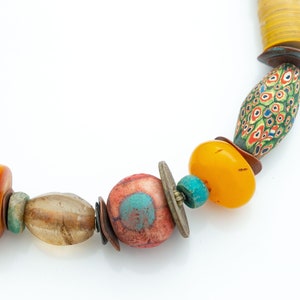 Peut inclure: Un collier coloré composé de différentes perles, dont de l'ambre, de la turquoise et du verre. Les perles sont enfilées sur un cordon et ont des formes et des tailles variées.