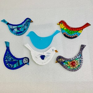 May include: Six mosaic bird ornaments in various colours and designs. The birds are made of small pieces of glass and tile, and they are all different shapes and sizes. The birds are arranged in a row on a white background.