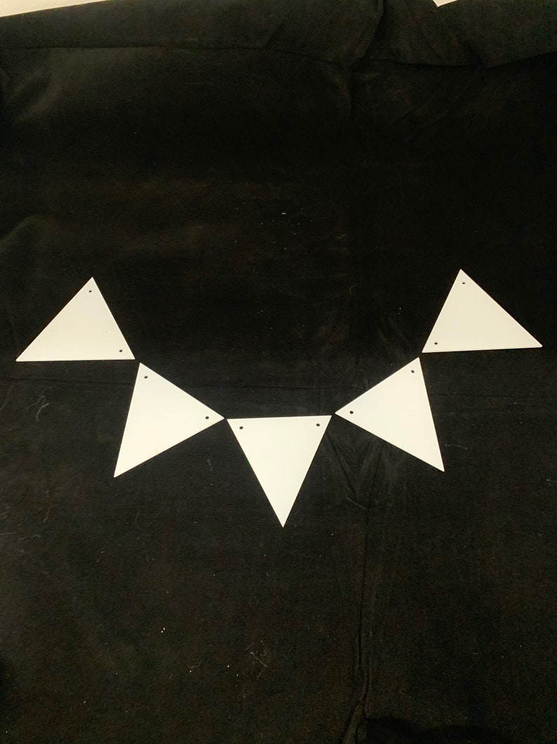 May include: A white triangle banner with six triangles connected together. The banner is hanging on a black fabric background.