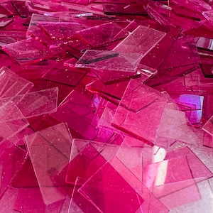 May include: A pile of pink, translucent glass shards. The shards are various sizes and shapes, creating a textured and colourful background.