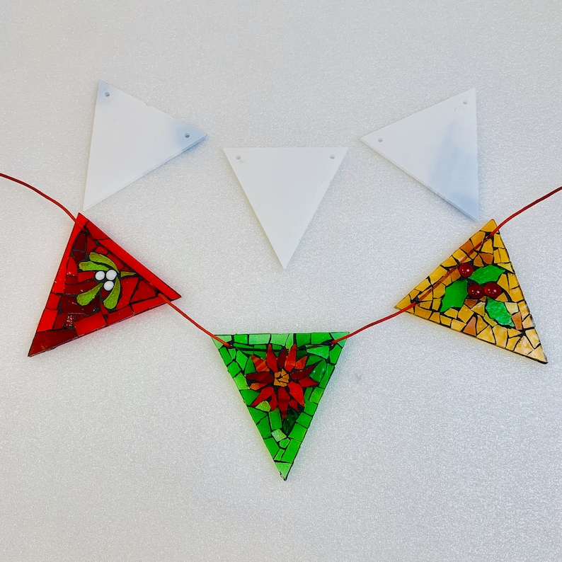 May include: A red, green and gold mosaic Christmas garland with a red holly berry, a green poinsettia and a gold holly berry design. The garland is strung on white string and is ready to be hung.