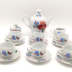 May include: A white porcelain tea set with floral designs. The set includes a teapot, sugar bowl, creamer, and six teacups and saucers. The floral designs are in shades of blue, red, and yellow.