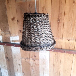 May include: A woven wicker lampshade hanging from a ceiling, with a wooden background.