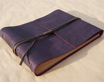 May include: A deep purple leather-bound photo album with a brown leather strap and knot closure. The album is personalized with the text "Our Adventures Zach & Emily".
